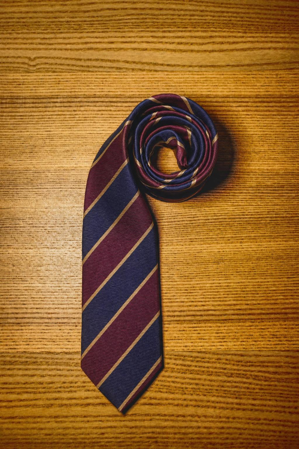 A burgundy and navy repp-stripe silk tie, rolled, on a wooden surface