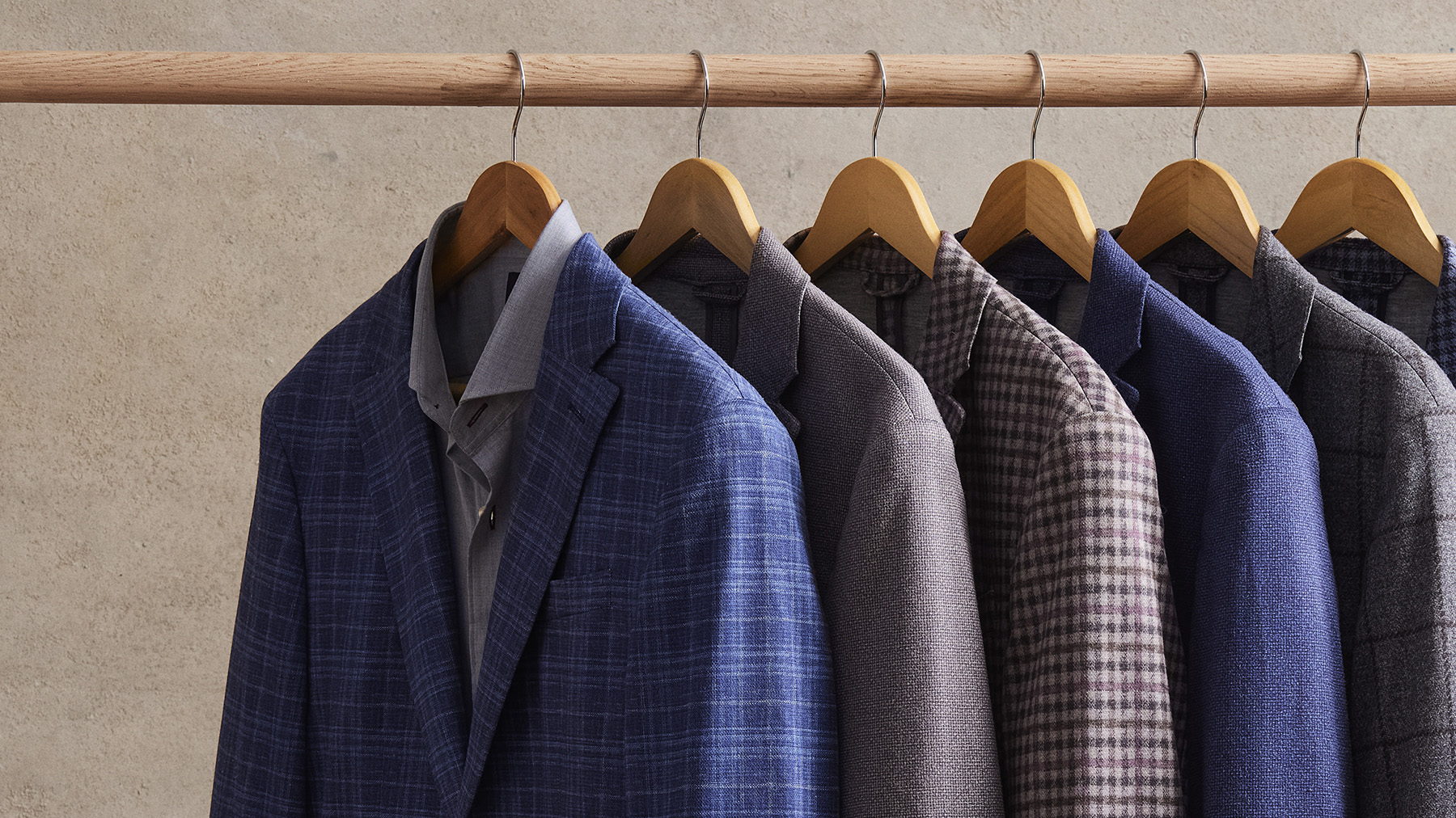 Sport coats hanging in good order along a wooden rail