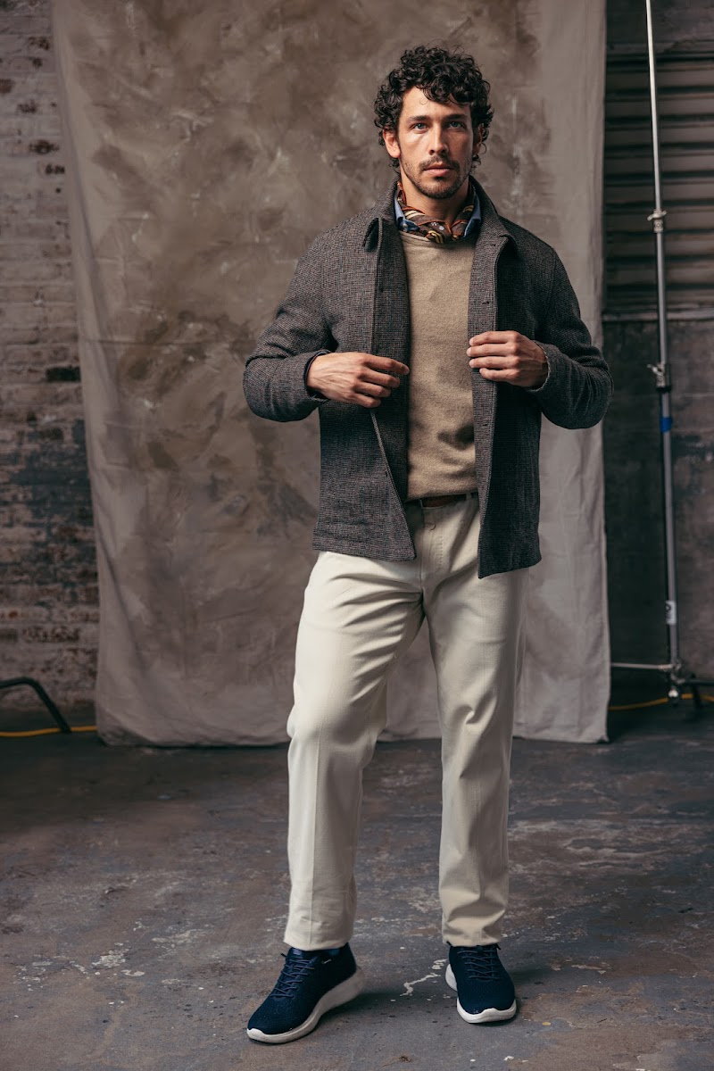 A textured knit sport jacket worn open over a sweater with cream trousers