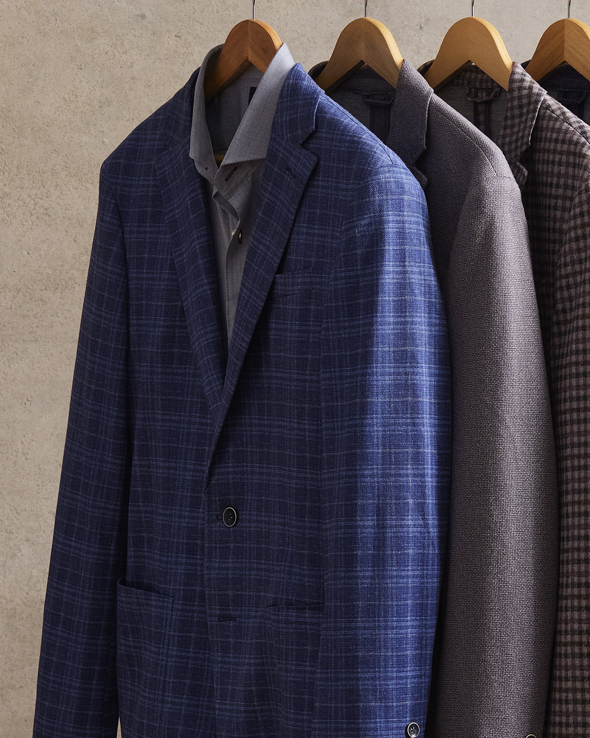 Sport coats on a rail in blue check, grey, and brown gingham, shoulder to hem